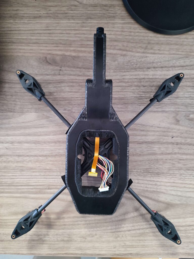Châssis du drone démonté : bras en croix et nappe de connexion vers la navboard, posé sur une table