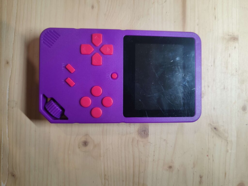 Console rétro violette vue de face, avec écran TFT éteint et boutons roses, avant le démontage